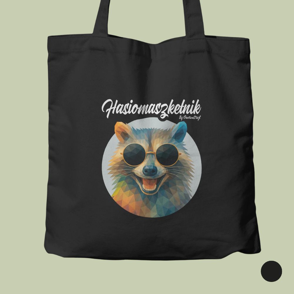 Czarna bawełniana torba ułożona płasko na szałwiowym tle. W centrum torby znajduje się okrągła, kolorowa ilustracja w stylu low-poly przedstawiająca uśmiechniętego szopa pracza w ciemnych okularach przeciwsłonecznych. Nad okręgiem umieszczono stylizowany biały napis „Hasiomaszketnik”. W prawym dolnym rogu zdjęcia znajduje się czarny okrąg oznaczający opcję kolorystyczną.