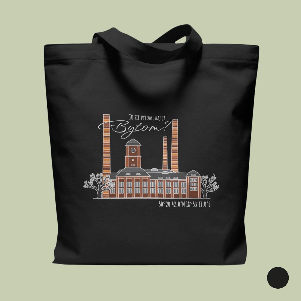 Czarna bawełniana torba na zakupy ułożona płasko na szałwiowym tle. W centrum torby znajduje się ilustracja przedstawiająca industrialny budynek z cegły z wieżą zegarową i trzonami kominowymi, ujęty między dwoma konturowymi drzewami. Nad budynkiem umieszczono biały napis „JO SIE PYTOM, KAJ JE Bytom?”, a poniżej współrzędne geograficzne „50°20'42.0"N 18°53'11.0"E”. W prawym dolnym rogu widoczny jest czarny okrąg oznaczający opcję kolorystyczną.