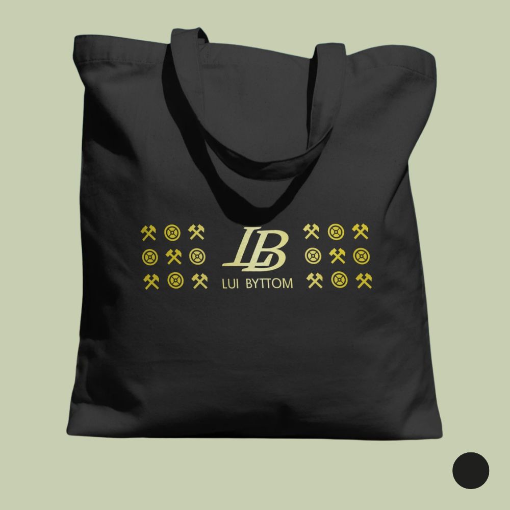Czarna bawełniana torba ułożona płasko na szałwiowym tle. W centralnej części torby znajduje się złoty nadruk składający się z monogramu „LB” i napisu „LUI BYTTOM”, otoczonego po bokach geometrycznym wzorem z miniaturowych symboli górniczych (skrzyżowane pyrlik i żelazko) oraz kół zębatych. W prawym dolnym rogu umieszczono czarny okrąg sygnalizujący dostępny wariant kolorystyczny.