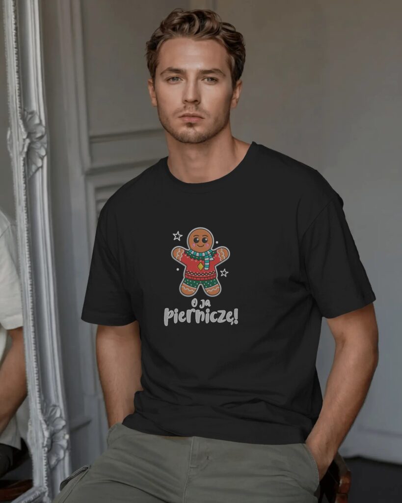Mężczyzna o krótkich, lekko falowanych włosach, stojący we wnętrzu z ozdobną lustrzaną ramą w tle. Ma na sobie czarny T-shirt oraz zielone spodnie cargo. Na piersi koszulki znajduje się nadruk z rysunkiem świątecznego piernikowego ludzika w szaliku oraz polskim napisem „O ja Pierniczę!”.