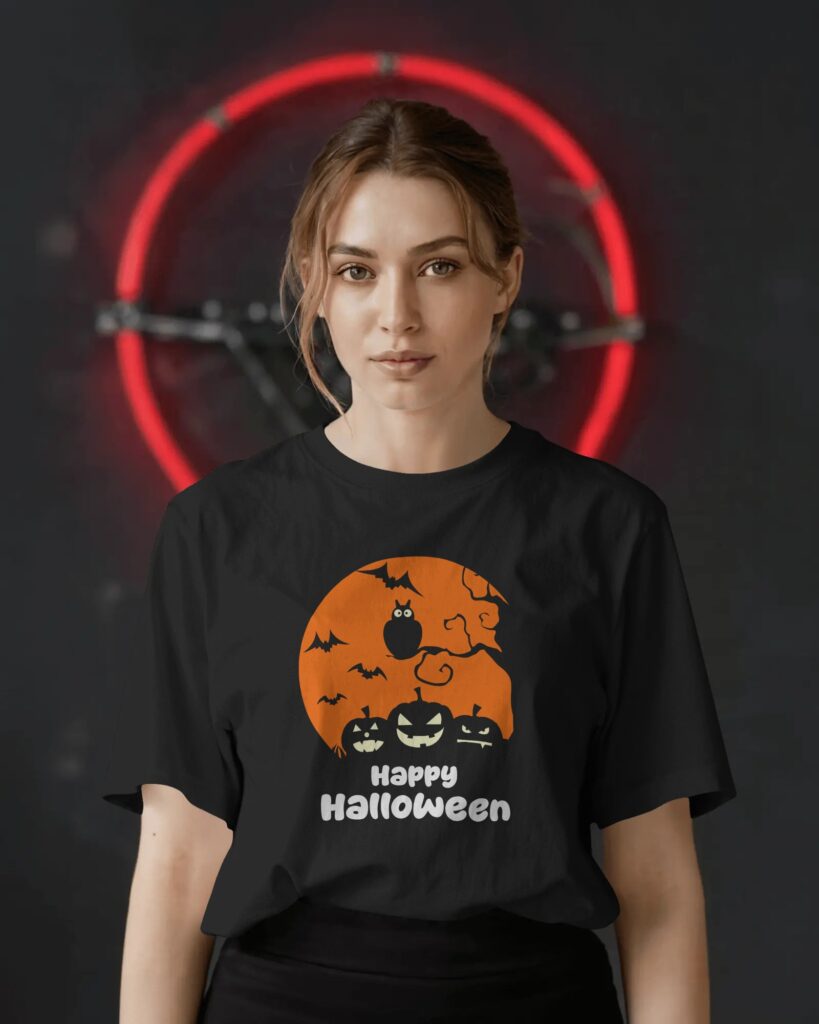 Młoda kobieta o spiętych włosach, stojąca na czarnym tle z rozświetlonym, czerwonym kołem neonowym umieszczonym za jej głową. Ma na sobie czarny T-shirt z halloweenowym nadrukiem – pomarańczowym księżycem z nietoperzami, sową oraz dyniami, pod którym znajduje się biały napis „Happy Halloween”.