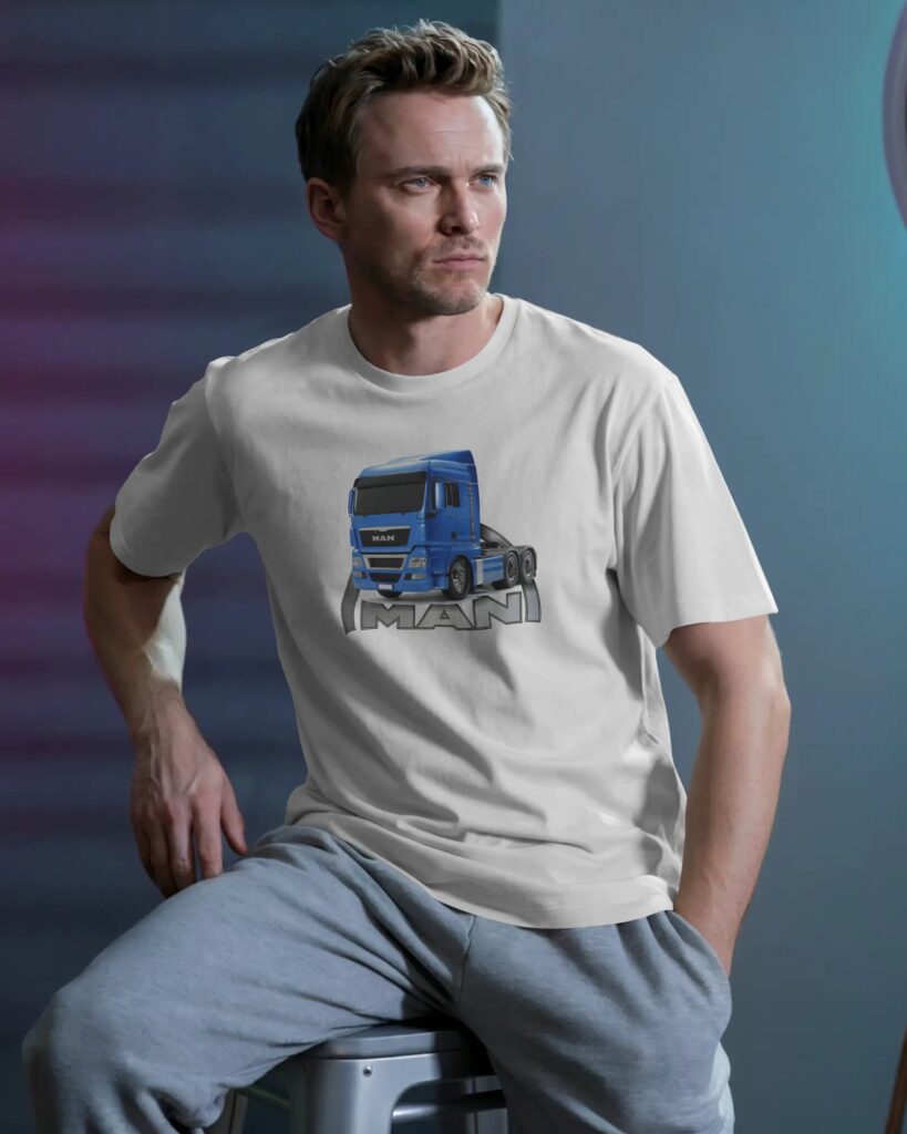 Mężczyzna o blond włosach siedzi na metalowym stołku z ręką w kieszeni szarych spodni dresowych. Ubrany jest w biały T-shirt z nadrukiem przedstawiającym niebieską ciężarówkę z napisem „MAN” na dole. Tło studio jest utrzymane w ciemnych, niebiesko-fioletowych tonacjach.