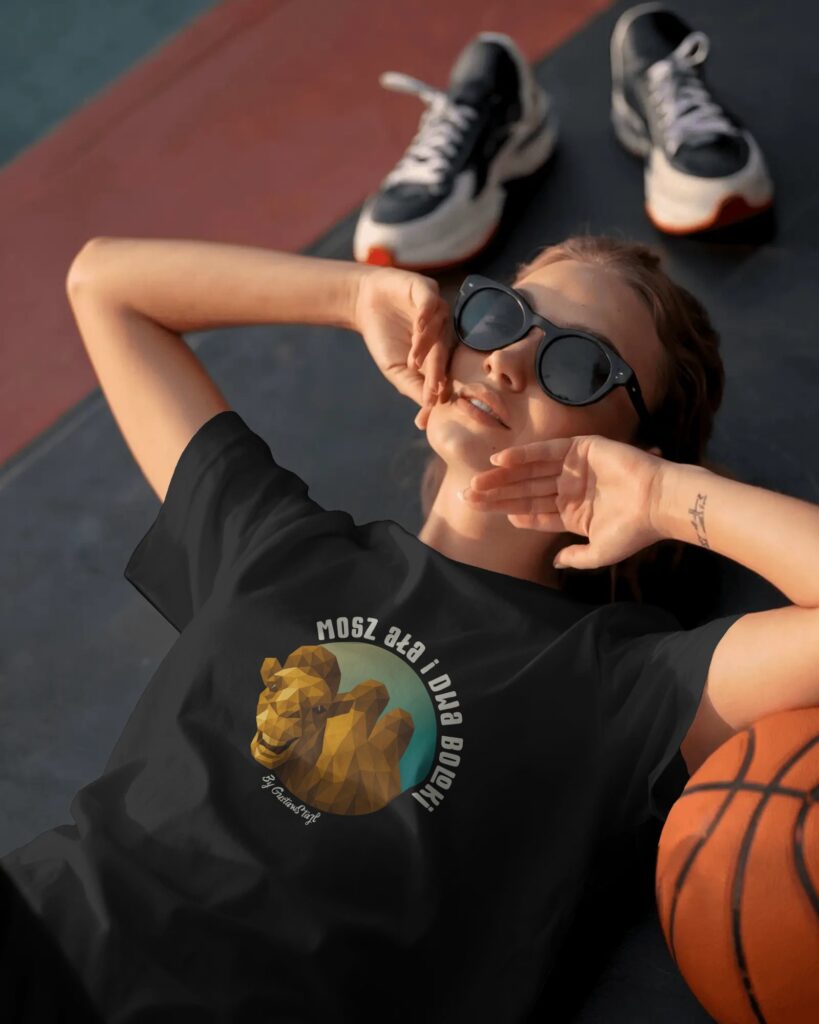 Młoda kobieta w czarnych okularach przeciwsłonecznych leżąca na podłożu boiska sportowego obok piłki do koszykówki. Ubrana jest w czarny T-shirt z barwną grafiką przedstawiającą geometryczną, poligonową głowę wielbłąda dwugarbnego wpisaną w okrągłe tło, z umieszczonym półkoliście jasnym napisem: „MOSZ AŁA I DWA BOLOKI” oraz drobnym podpisem „by GustawStajl”.